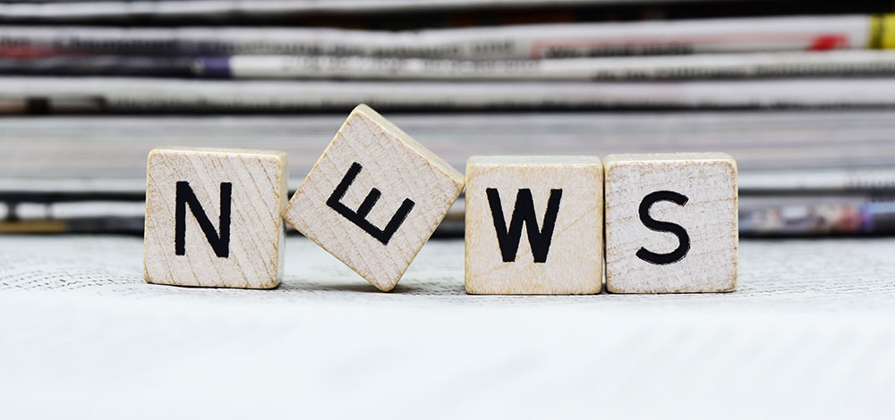 News spelled out on little blocks with newspapers behind