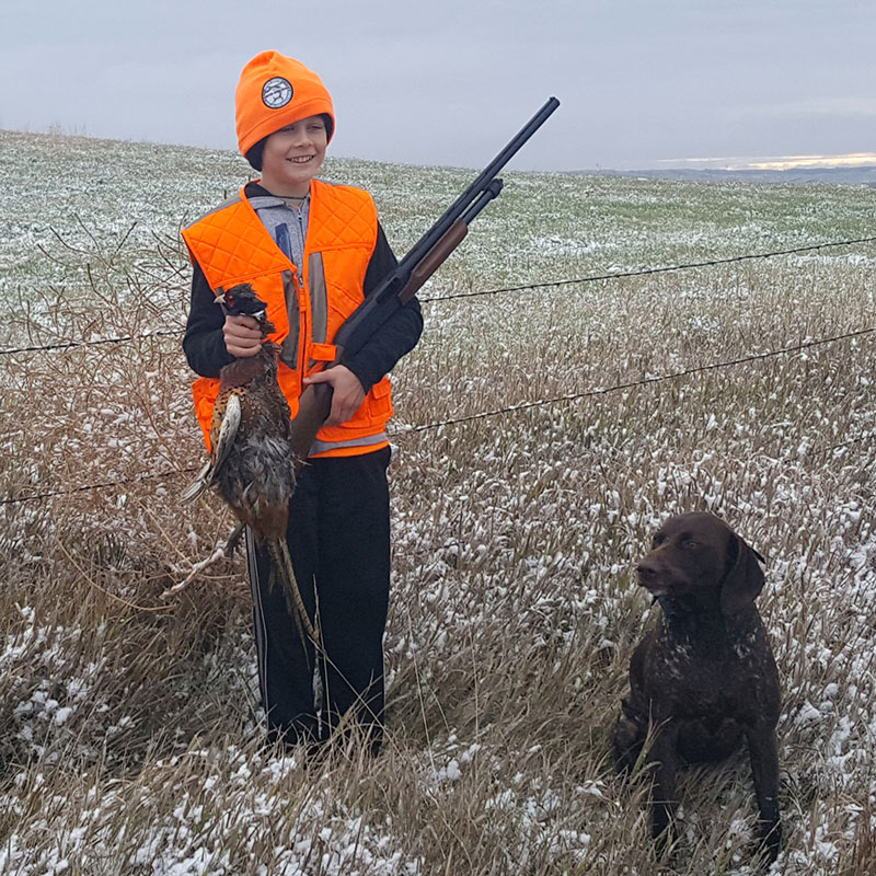 Kid holding pheasant he harvested with dog near