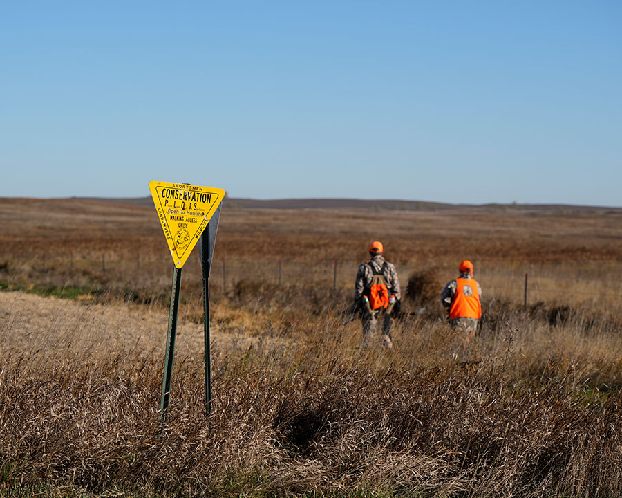 PLOTS sign in field with hunters in background