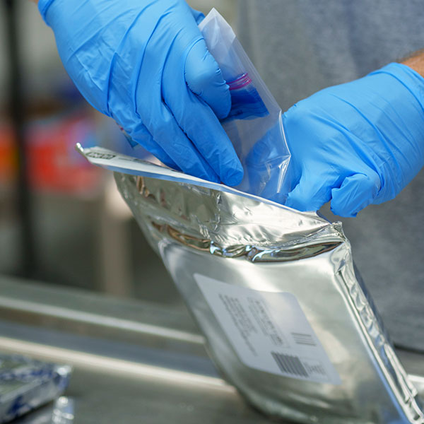 Person placing baggie with whirlpack into an insulated mailer envelope