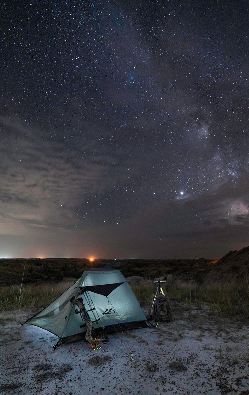 Tent in badlands with bow leaning on side and stars above