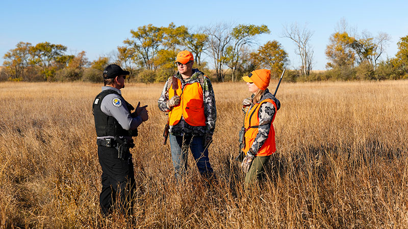 Warden talking to two hunters in the field