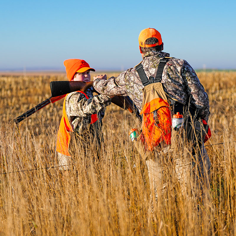 Father passing his gun to his son before he crosses a fence