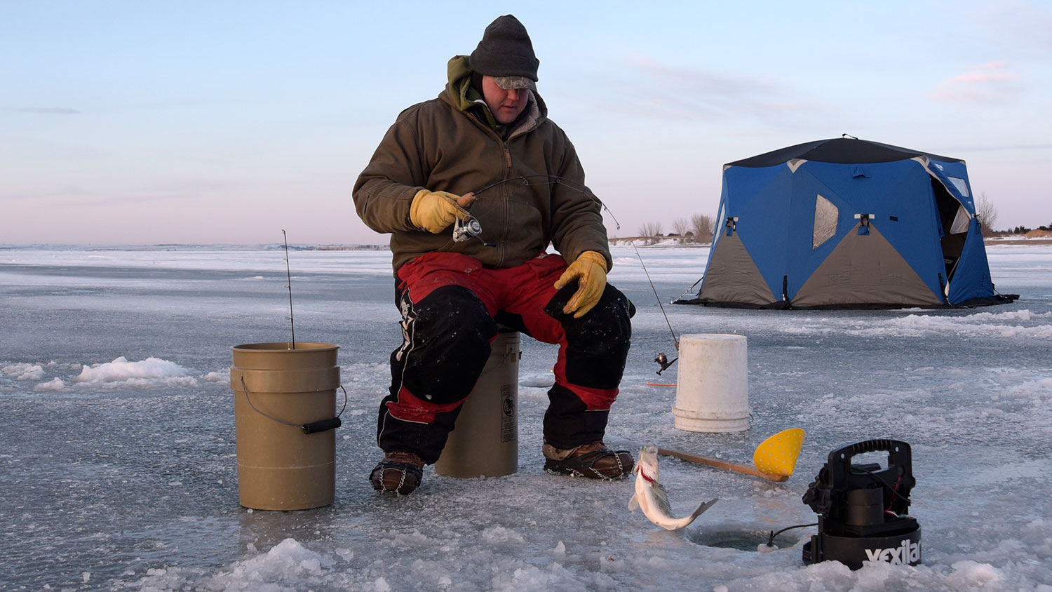 Man sitting on bucket ice fishing