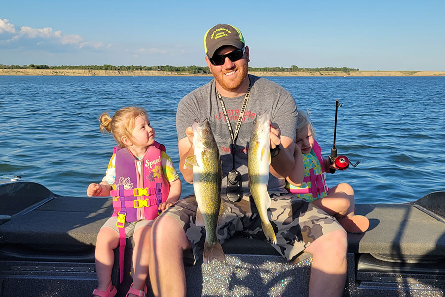 Father with his two daughters on a boat. Father is holding two fish they caught.
