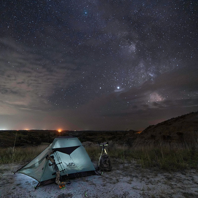 Lit tent in the badlands with stars above