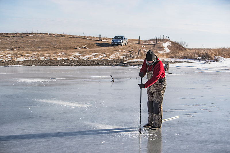 Angler drilling hole in ice