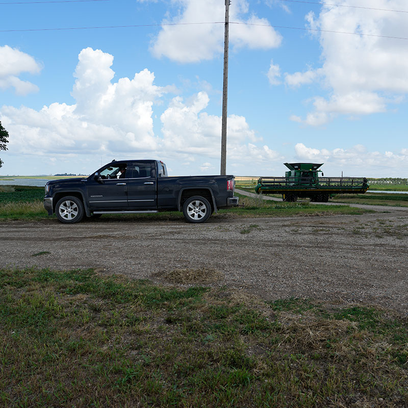 Truck parked on side of gravel road with farm machinery approaching