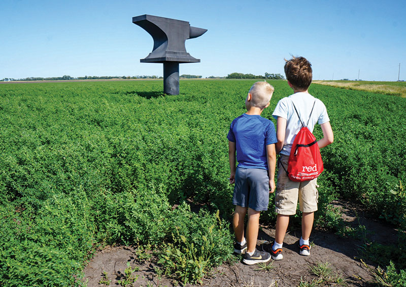 Kids looking at anvil sculpture in crop field