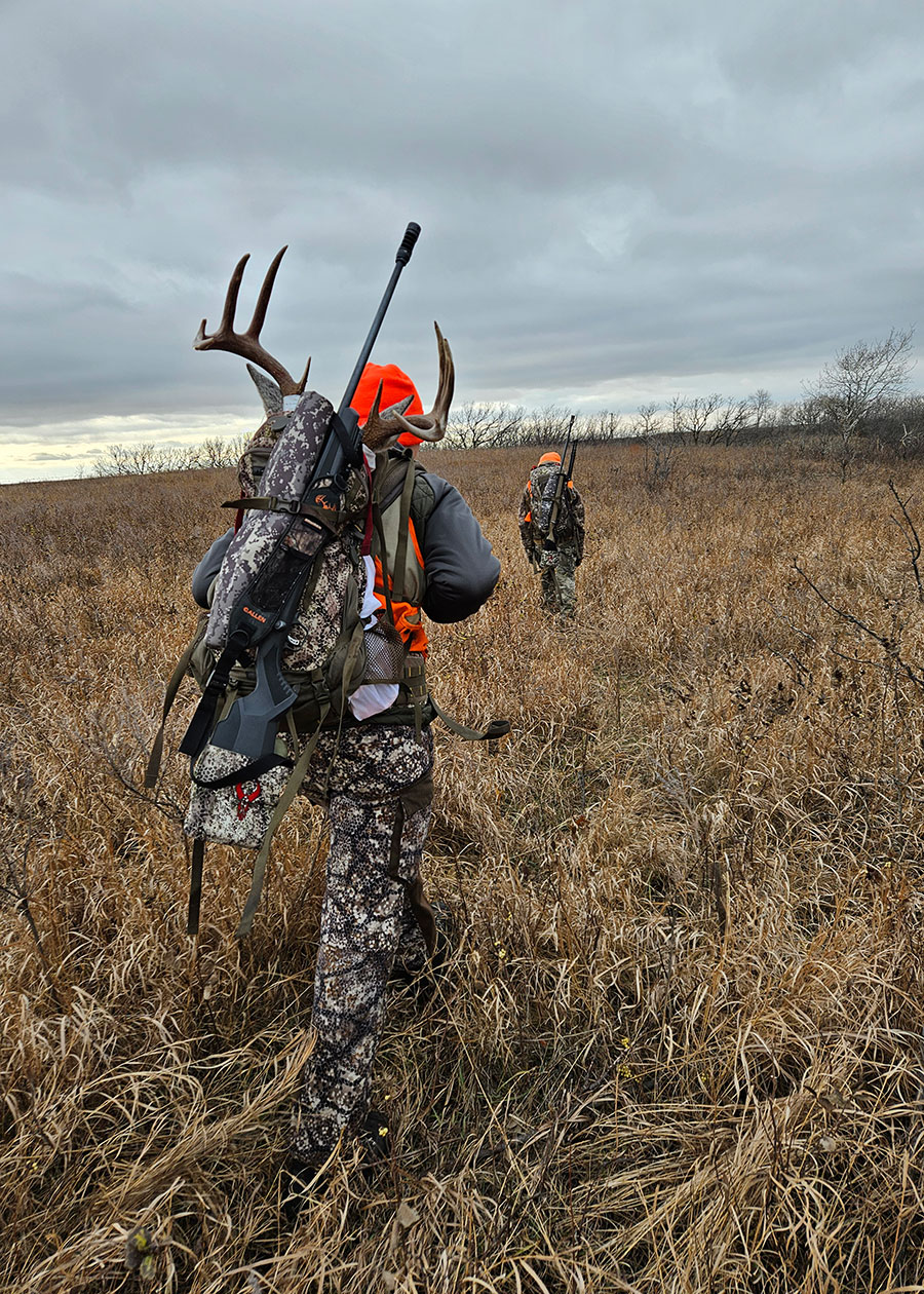 Two hunters walking in a field, one carrying antlers