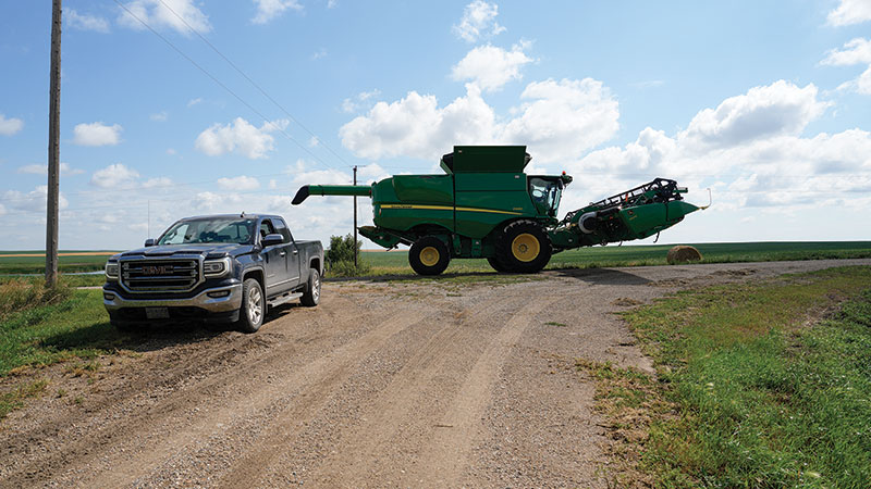 Truck on side of gravel road with farm machinery behind it