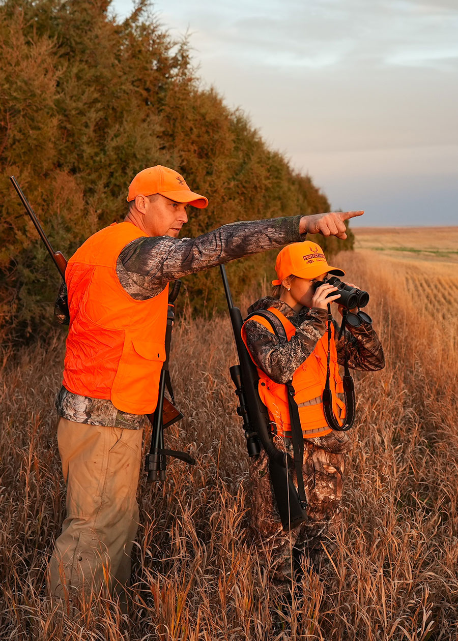 Father and daughter deer hunting near tree row and crop field