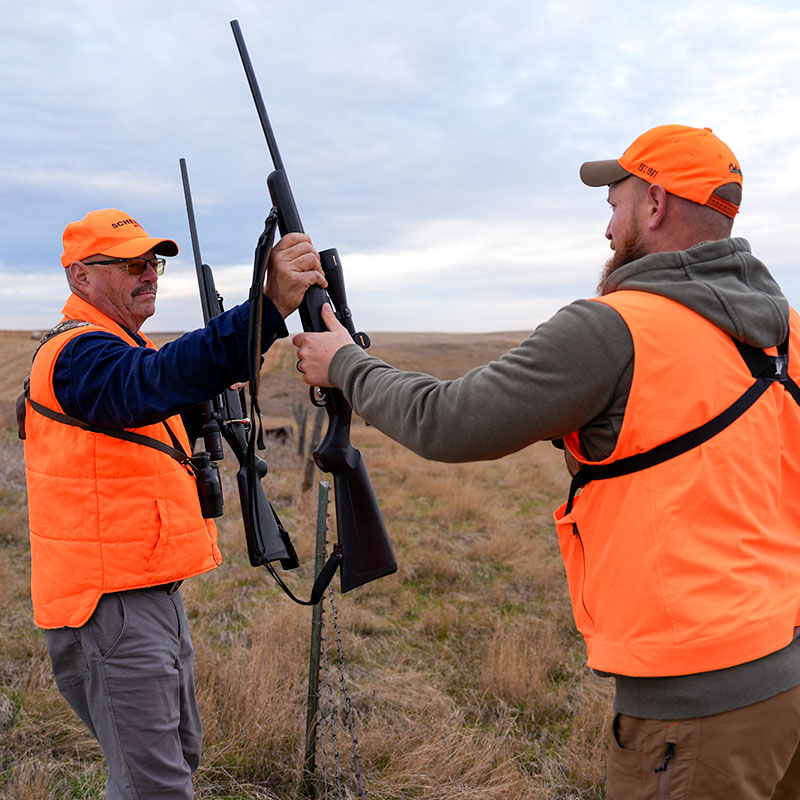 Hunters in the field passing a gun over a fence