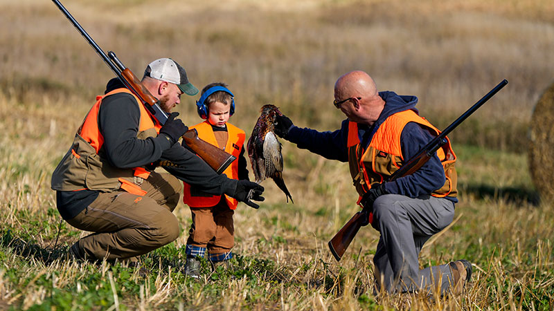 Two upland game hunters showing a child the pheasant they harvested
