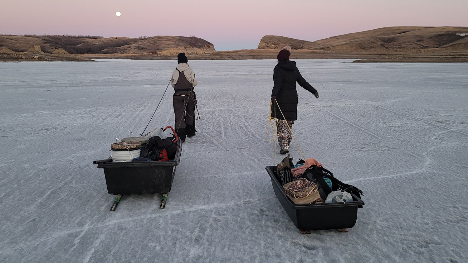 Women pulling sleds with fishing gear out on ice to go fishing