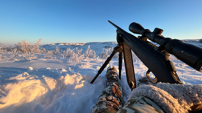 Hunter sitting in snow with rifle on sticks