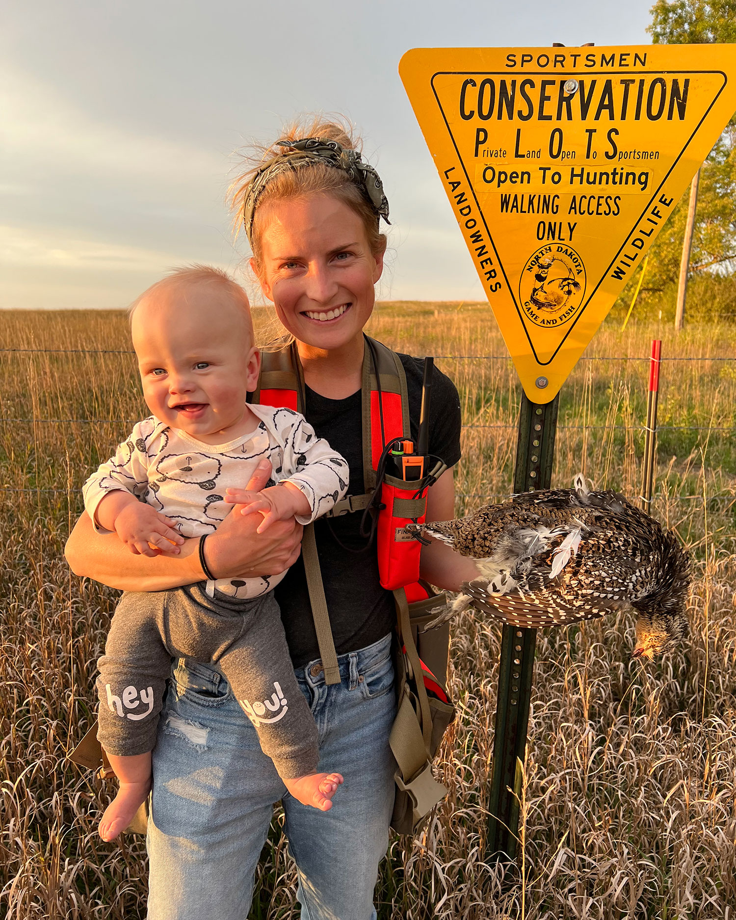 Fich and Cayla by a PLOTS sign with Cayla holding a harvested sharptail