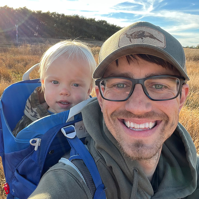 Scott with son in backpack in the field