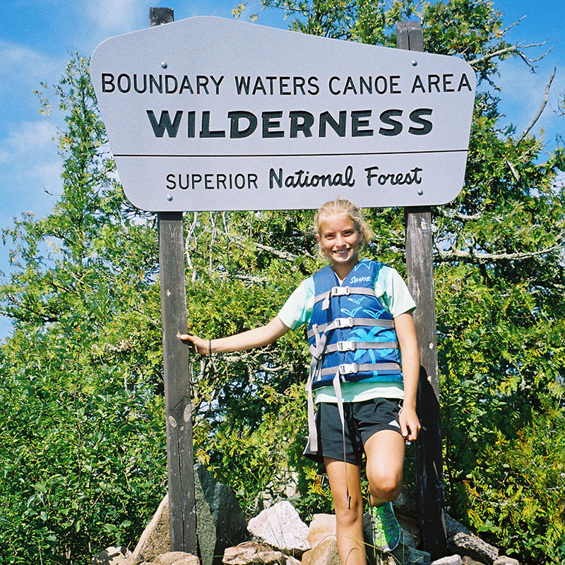 Author as a child wearing a life jacket standing by a wilderness sign