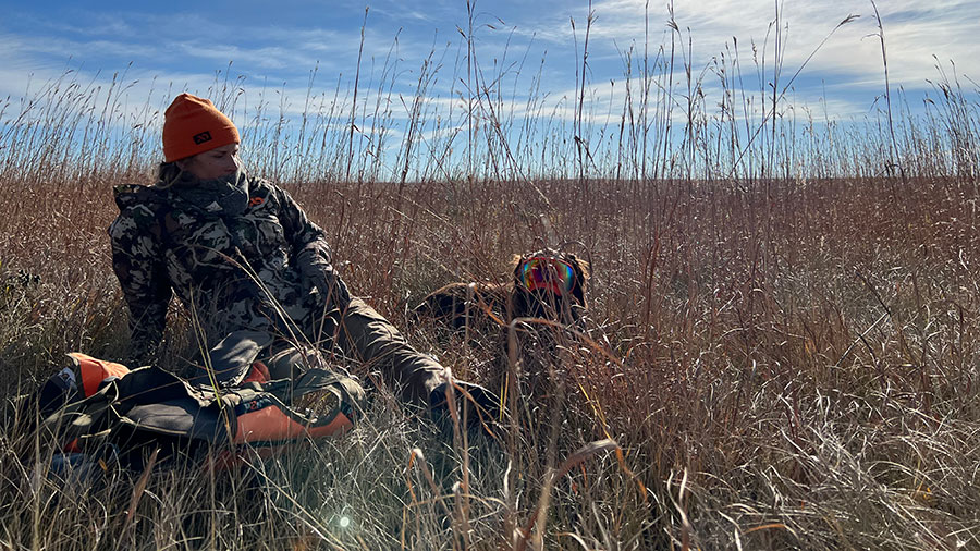 Woman and dog in tall grass taking a break while hunting