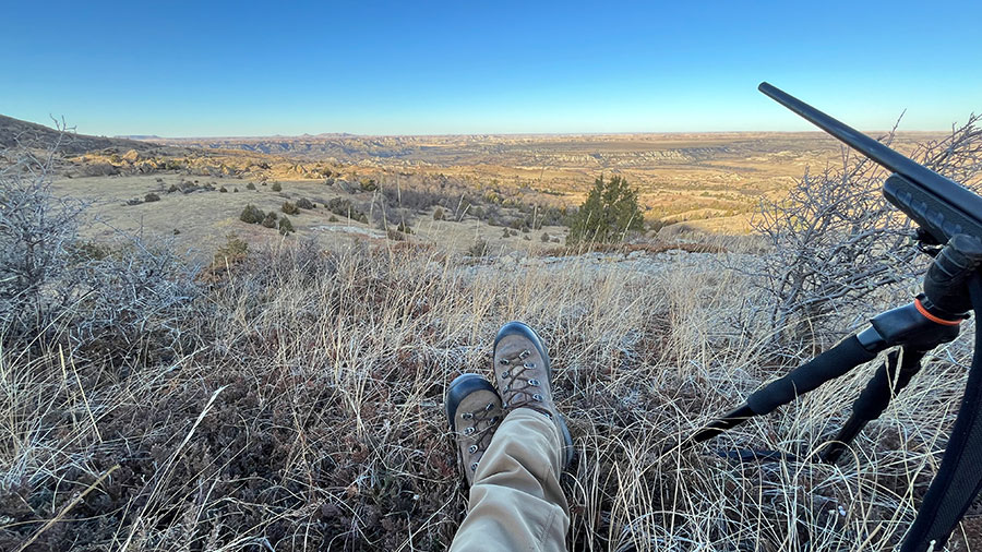 Looking out over badlands with feet of a sitting hunter showing and a rifle to the side