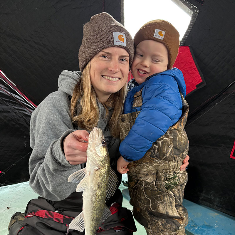 Cayla holding a walleye while hugging Fischer in the ice house