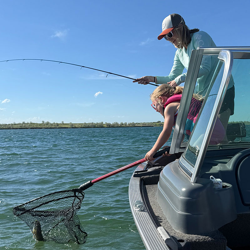 Angler reeling in fish from boat with child holding the net