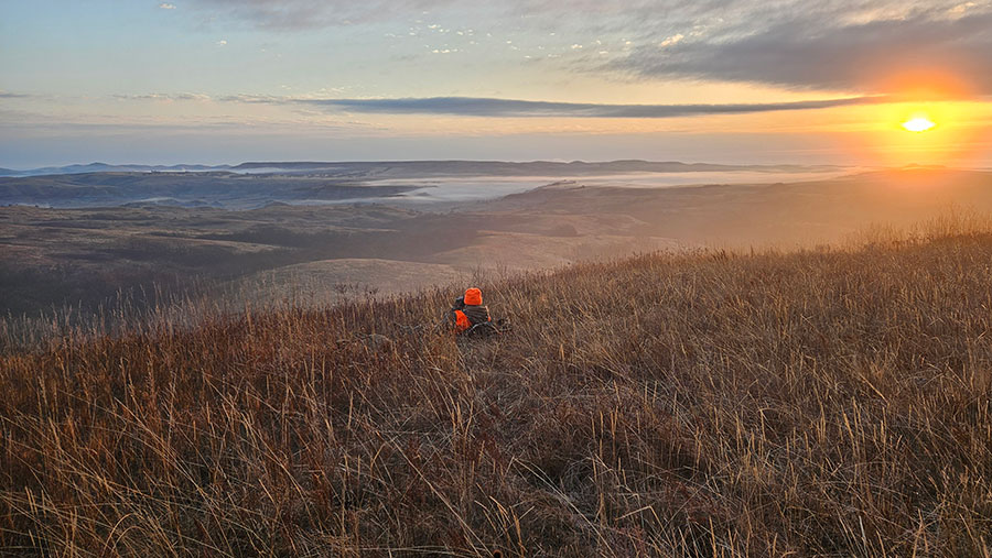 Hunter sitting on hill at sunrise