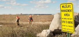 WMA sign with hunters in field behind