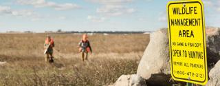 WMA sign with hunters in field behind