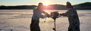 Women using auger to drill hole in lake ice