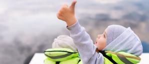 Child in boat with lifejacket on doing a "thumbs-up" sign