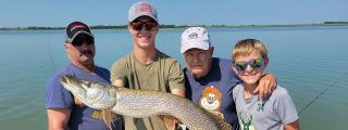 Four anglers on a boat with a pike they caught