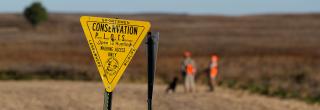 PLOTS sign with hunters in the background