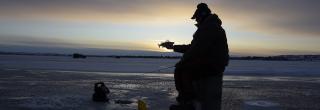 Person sitting on bucket ice fishing