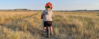 Child riding bike down dirt track in the prairie