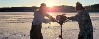 Women using auger to drill hole in lake ice