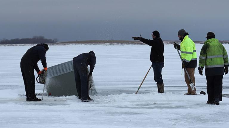 People working on getting an ice house and truck out of the water