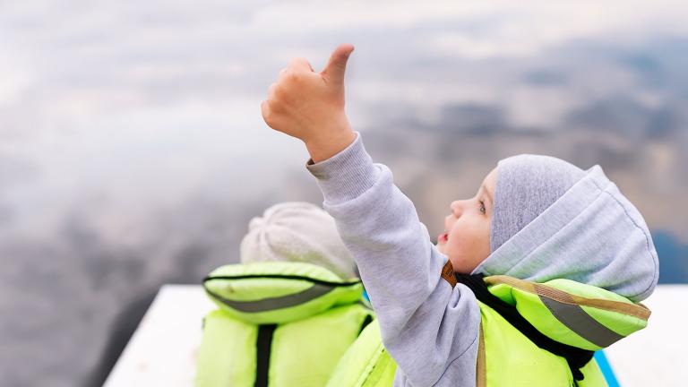 Child in boat with lifejacket on doing a "thumbs-up" sign