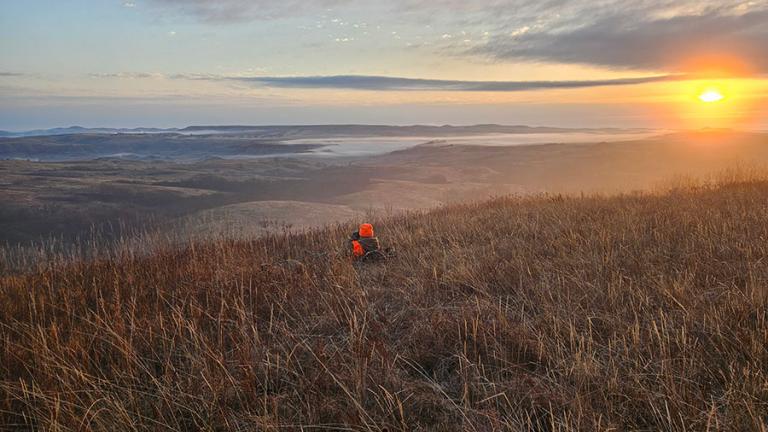Hunter sitting on hill at sunrise