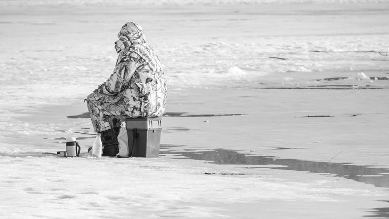 Angler ice fishing with melted ice behind him