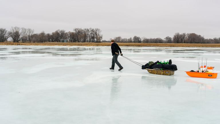 Person pulling sleds filled with ice fishing equipment across an iced over lake