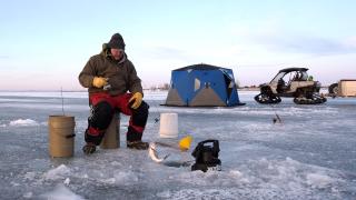 Man sitting on bucket ice fishing