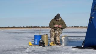 Ice angler sitting on bucket on frozen lake