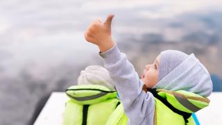 Child in boat with lifejacket on doing a "thumbs-up" sign