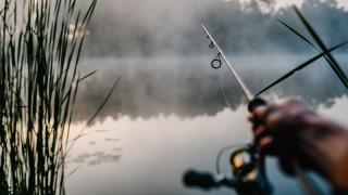 Hands holding fishing pole at foggy pond