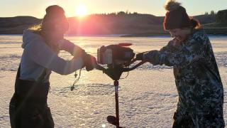 Women using auger to drill hole in lake ice
