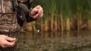 duck hunter holding decoy weight with weeds stuck to it